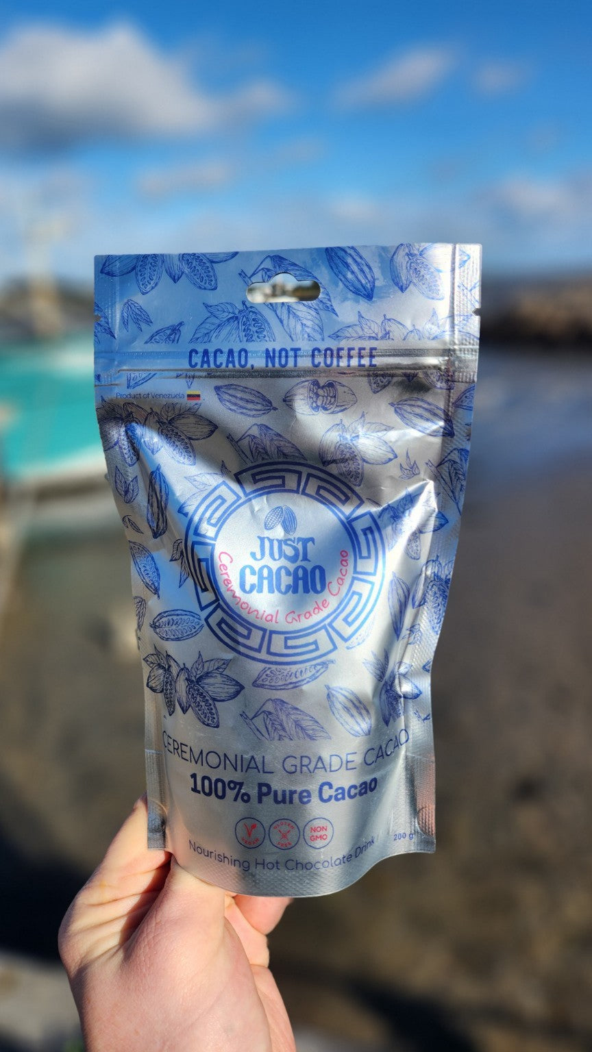 Just Cacao Venezuelan ceremonial cacao pouch held beside a sunny harbour.