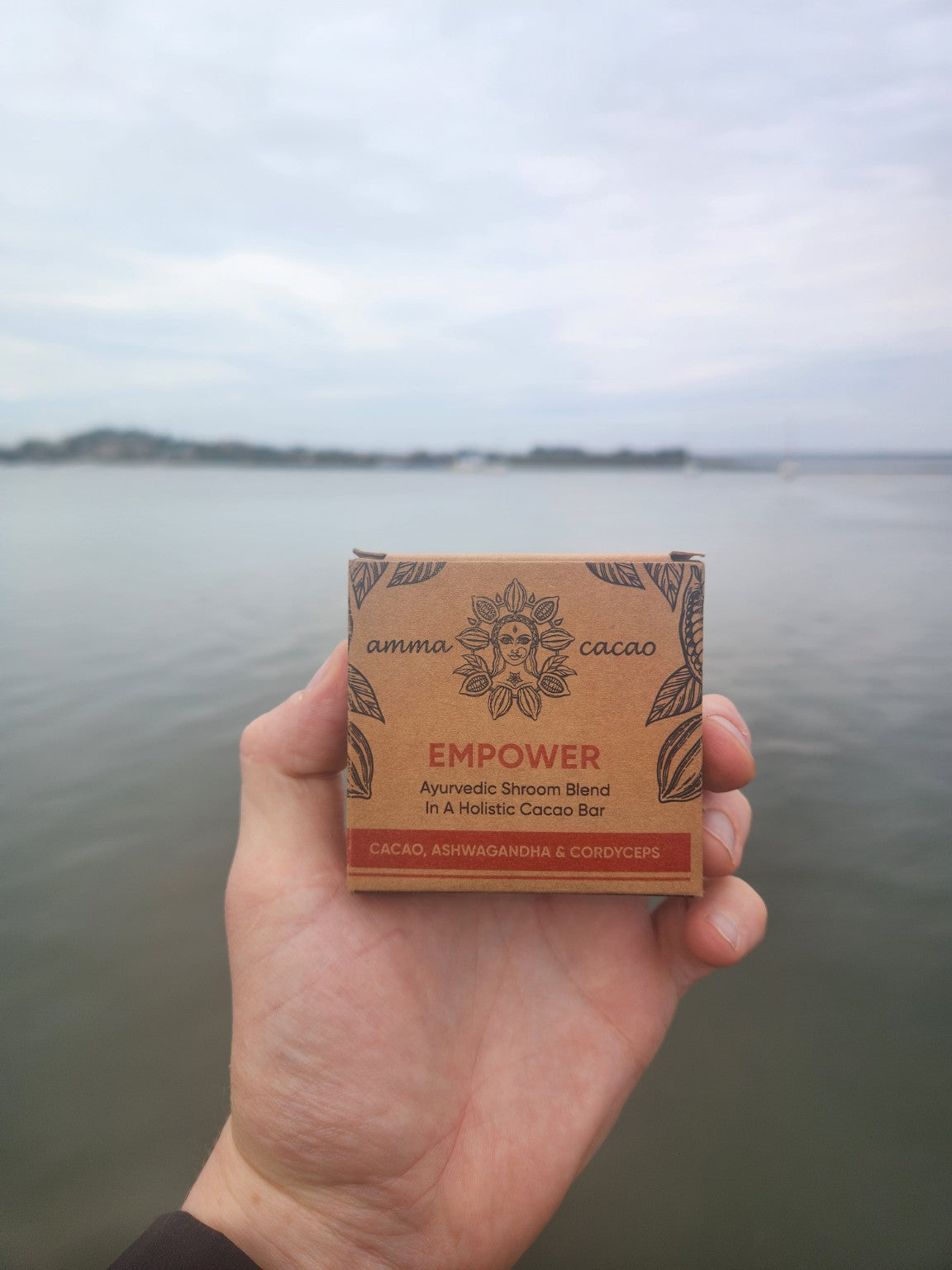 Amma HEAL 36g cacao bar held beside the water, photographed by Mother Earth